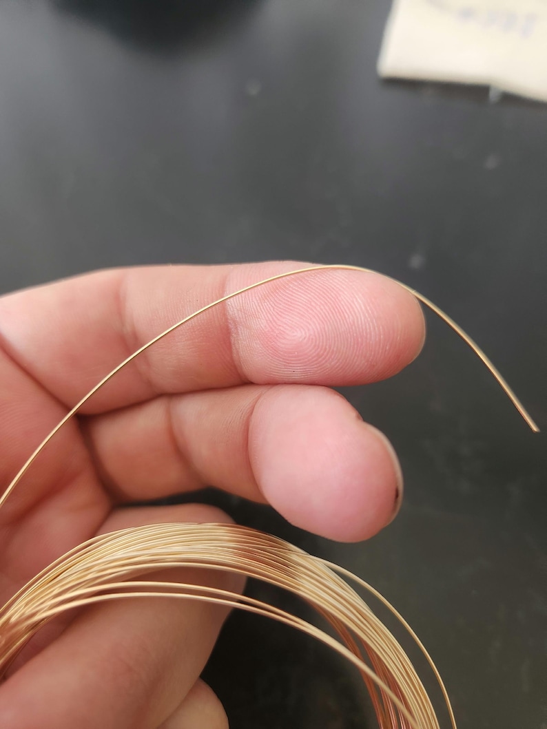 May include: A close-up of a spool of gold-colored wire. The wire is thin and appears to be made of metal.