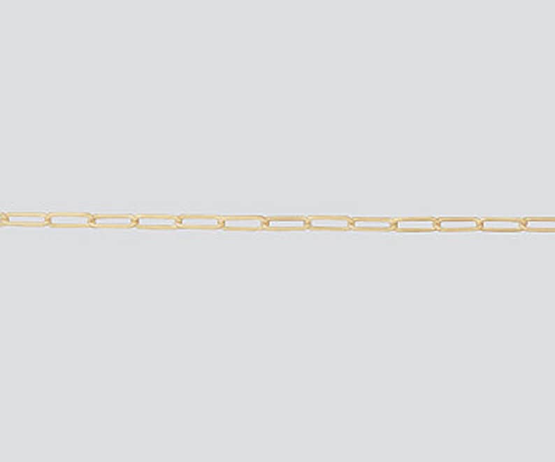 May include: A delicate gold-colored chain necklace with rectangular links. The chain is displayed against a plain, light gray background, highlighting its simple design and metallic sheen. The links are evenly spaced, creating a linear pattern.