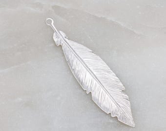 Op de afbeelding: Een zilveren veerbedel met een gedetailleerd, gestructureerd ontwerp. De bedel heeft een lus aan de bovenkant om aan sieraden te bevestigen.