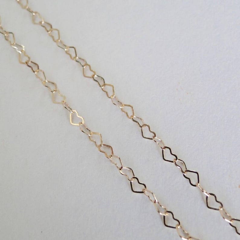 K&ouml;nnte beinhalten: Zwei Str&auml;nge einer goldenen herzf&ouml;rmigen Kette, &uuml;bereinander, vor einem wei&szlig;en Hintergrund.
