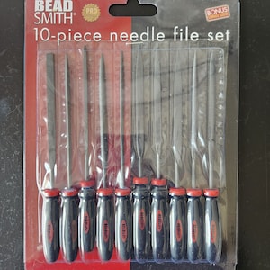 Peut inclure: Un ensemble de 10 limes aiguilles de Bead Smith. L'ensemble comprend dix limes métalliques avec des manches noirs et des embouts rouges, emballées dans une pochette en plastique transparent. Le paquet porte l'inscription "10-piece needle file set".