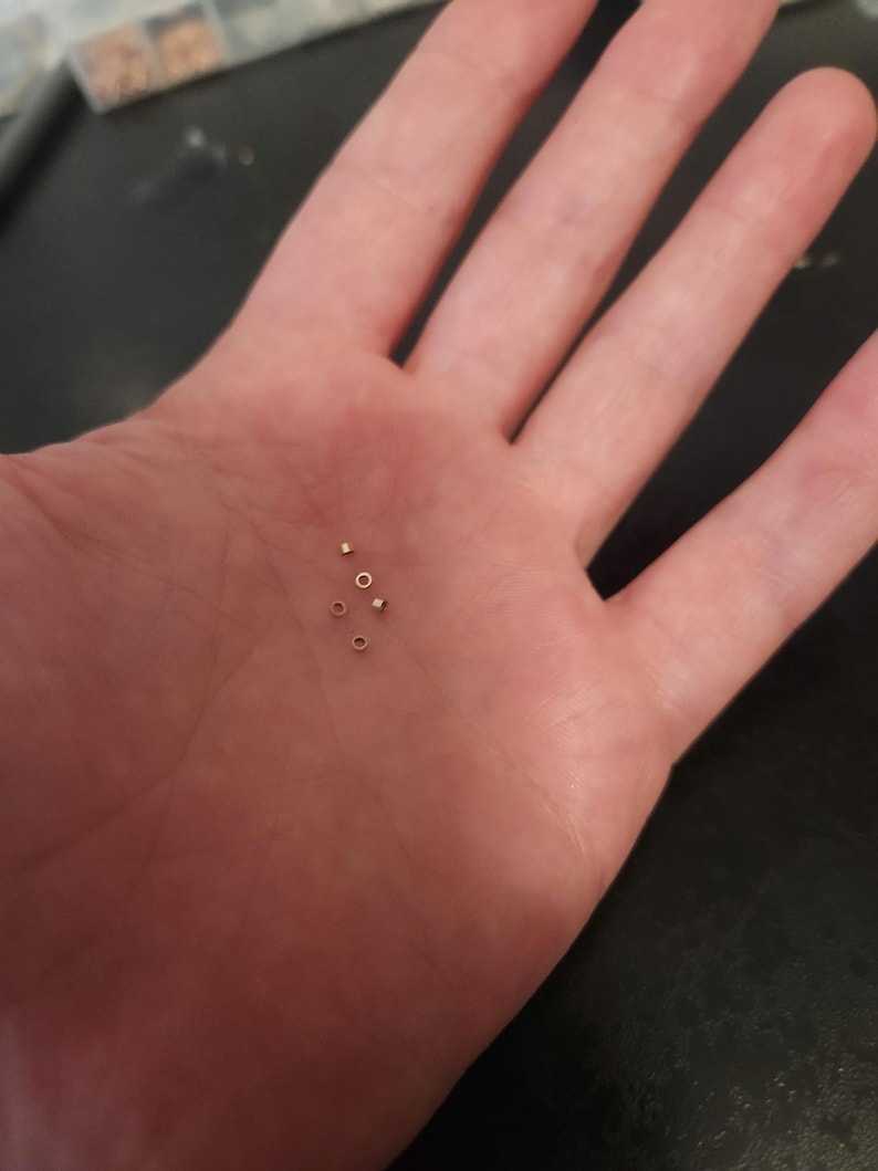 May include: A close-up of a hand holding six small, gold-coloured jump rings.