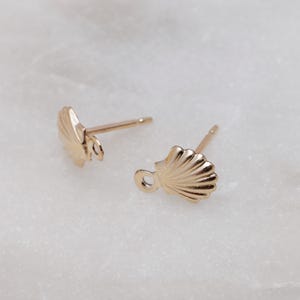 May include: A pair of gold-toned seashell stud earrings. Each earring features a detailed seashell design with a small loop on the back.