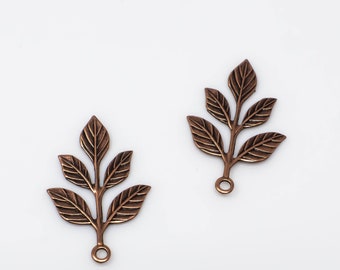 May include: Two bronze-colored leaf charms with detailed veining. Each charm features a stem with three leaves and a small loop at the base for attaching to jewelry or other crafts. The charms are set against a white background.