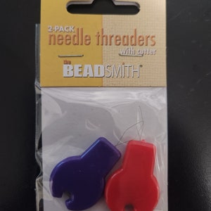 May include: Two-pack of needle threaders with cutters. The threaders are purple and red and have a loop at the end. The packaging says "the Beadsmith" and "2-pack needle threaders with cutter".