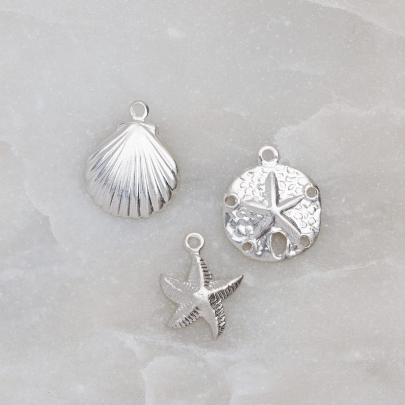 May include: Three silver charms in the shape of a seashell, a starfish, and a sand dollar.