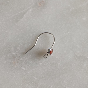 May include: A silver earring with a small red gemstone.