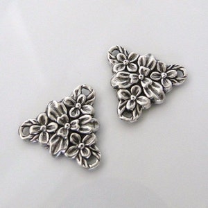 May include: Two silver-toned metal triangle-shaped charms with a floral design. Each charm has three loops for attaching to jewelry or other crafts.