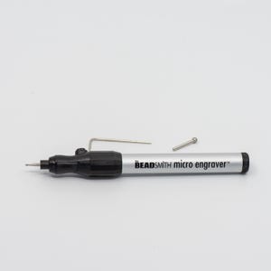 May include: A silver and black Beadsmith micro engraver tool with a small metal bit attached. The tool is on a white surface with two small metal pieces next to it.