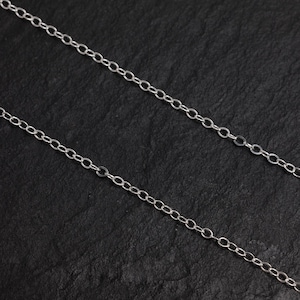 May include: A silver chain necklace with a delicate, oval-shaped link design. The chain is displayed on a black background.