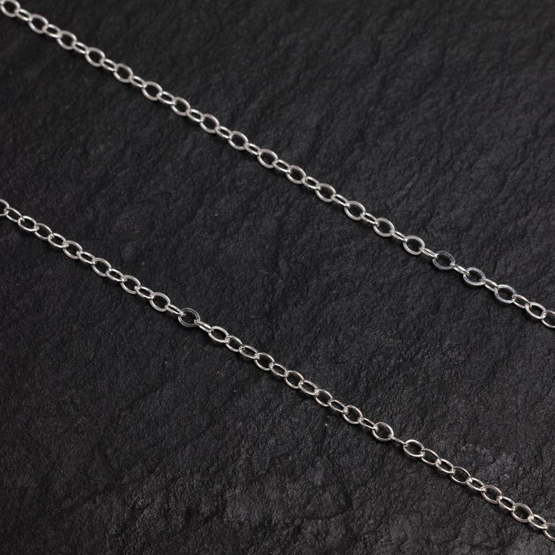 May include: A silver chain necklace with a delicate, oval-shaped link design. The chain is displayed on a black background.