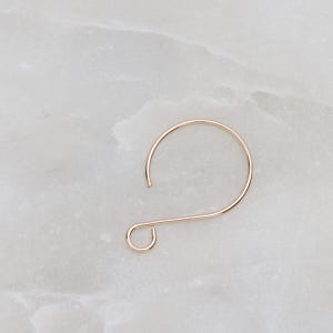 May include: A gold-toned metal earring hook with a simple, curved design.