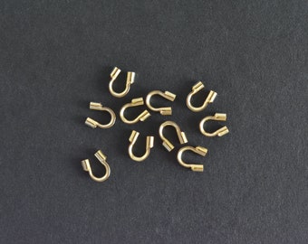 May include: A group of gold-colored metal crimp beads, also known as crimp covers, are scattered on a black surface. These beads are used to secure jewelry findings and create a professional finish.