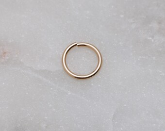 Könnte beinhalten: Ein goldfarbener nahtloser Creolenohrring. Der Creolenohrring ist glatt und hat eine polierte Oberfläche.