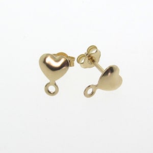 May include: A pair of gold-colored heart-shaped stud earrings. Each earring features a rounded heart design with a small loop at the bottom. The earrings are displayed against a white background, highlighting their polished finish.