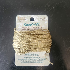 May include: A spool of gold-colored waxed Brazilian cord, labeled "Knot-it!" by Bead Smith. The label indicates 15 yards (4.5m) of cord, perfect for jewelry, macrame, and crafts. The packaging includes text in English, French, and Spanish.