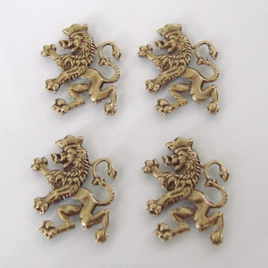 Può includere: Quattro applicazioni a forma di leone color oro antico. Ogni leone è in posa araldica, con corona e criniera dettagliata. Le applicazioni sono su sfondo bianco, mettendo in risalto il loro design intricato e la finitura metallica.