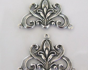 May include: Two silver-toned metal decorative embellishments with a floral design. Each embellishment has a triangular shape with a central floral motif and intricate scrollwork.