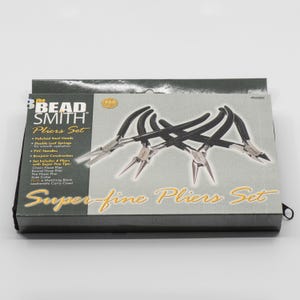 Puede incluir: Un juego de cuatro alicates de mango negro con puntas superfinas en una caja gris con el texto "the BEAD SMITH Pliers Set" y "Super-fine Pliers Set".