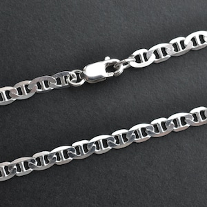 Könnte beinhalten: Eine silberfarbene Ankerkette mit einem Karabinerverschluss. Die Kette besteht aus ovalen Gliedern mit einem Steg in der Mitte jedes Glieds. Die Halskette wird vor einem dunklen Hintergrund gezeigt.