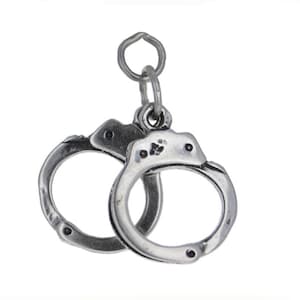 May include: Silver charm in the shape of handcuffs. The charm is designed to look like a pair of handcuffs, with two metal rings connected by a chain.