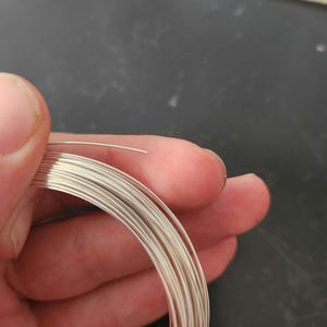 May include: A coil of silver wire, approximately 20 gauge, is held in a hand. The wire is shiny and has a smooth surface.