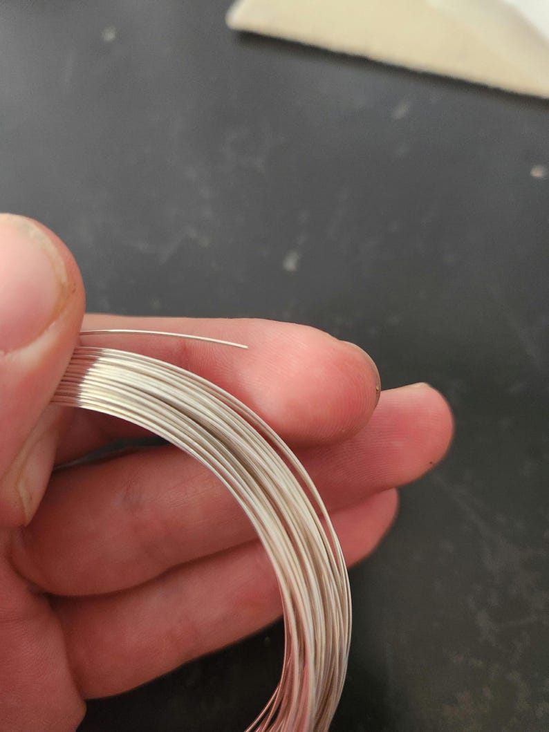 May include: A coil of silver wire, approximately 20 gauge, is held in a hand. The wire is shiny and has a smooth surface.