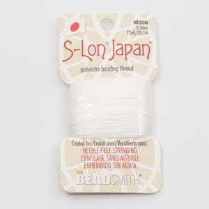 Op de afbeelding: Witte S-Lon Japan polyester rijggaren, medium 0,3 mm, 20,1 m, voor naaldloos rijgen. De verpakking heeft de merknaam en een Japans vlagontwerp. Het product is van Beadsmith.