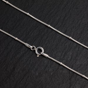 Puede incluir: Un collar de cadena de plata con un dise&ntilde;o delicado y con cuentas. La cadena es fina y tiene un aspecto simple y elegante.