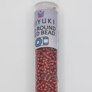 May include: A small clear tube filled with red round seed beads. The label on the tube reads "MIYUKI ROUND SEED BEAD".