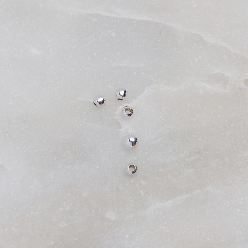 May include: Five silver round beads on a white background.