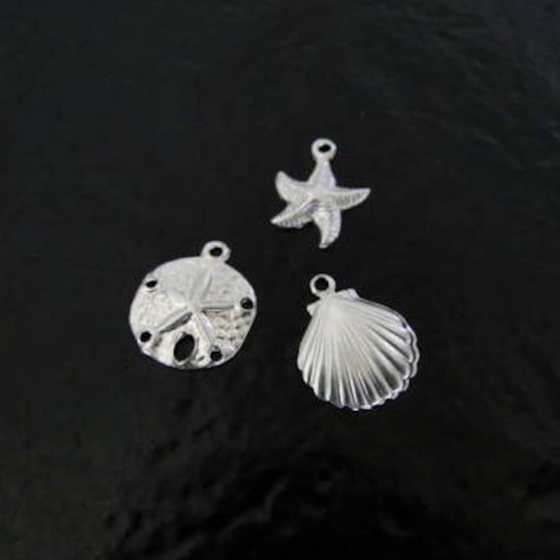 May include: Three silver charms in the shape of a seashell, a sand dollar with a starfish in the center, and a starfish.