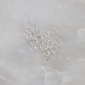 May include: A pile of silver jump rings, oval shaped, on a white marble surface.