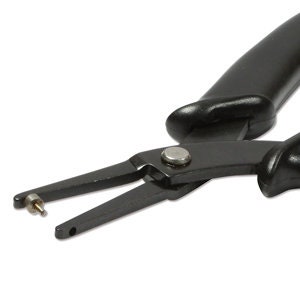 May include: Black metal pliers with a single hole punch. The pliers have a curved handle for grip and a silver rivet. The tool is designed for making holes in various materials.