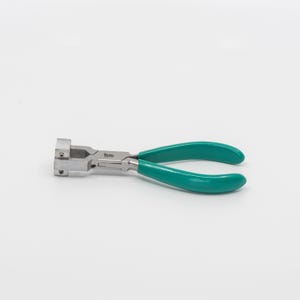 May include: A pair of silver-toned pliers with green handles. The pliers have a square jaw and are used for jewelry making.