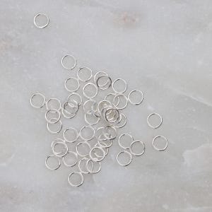 May include: A pile of silver jump rings, scattered on a white marble surface.