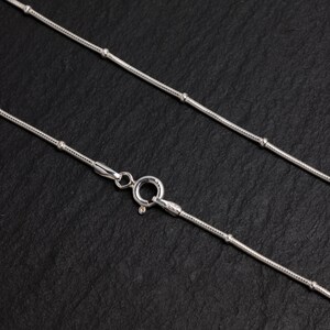 Puede incluir: Un collar de cadena de plata con un dise&ntilde;o delicado y con cuentas. La cadena es fina y tiene un aspecto simple y elegante.