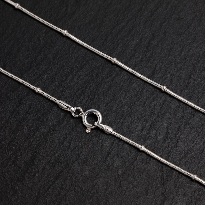 Puede incluir: Un collar de cadena de plata con un dise&ntilde;o delicado y con cuentas. La cadena es fina y tiene un aspecto simple y elegante.