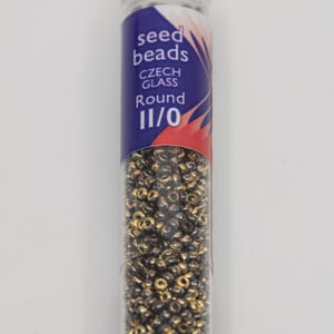 May include: A clear tube filled with small, round, gold and black seed beads. The tube has a label with the words "seed beads," "CZECH GLASS," and "Round 11/0" in white text on a blue background. The beads are densely packed.