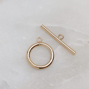 May include: Gold-toned metal toggle clasp with a round ring and a straight bar. The clasp is a jewelry finding used for necklaces, bracelets, and other jewelry.