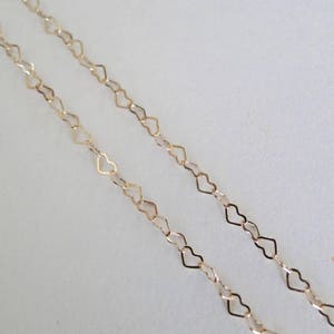 May include: Two strands of gold heart-shaped chain, one on top of the other, against a white background.