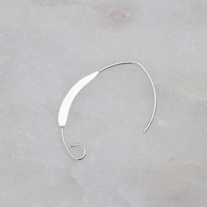 May include: A silver hoop earring with a unique curved design. The hoop is open and has a small loop at the end.