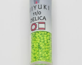 May include: A clear glass bottle filled with bright green seed beads. The label on the bottle reads "MIYUKI 11/0 DELICA" with a small crown logo above the text.