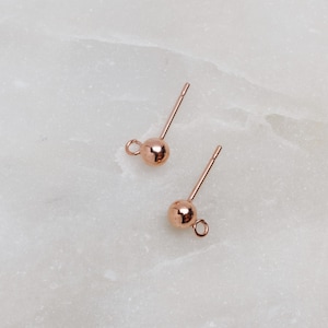 May include: Two rose gold earring posts with a small ball at the end and a loop at the top.