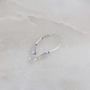 Puede incluir: Gancho para pendientes de plata con un diseño curvo. El gancho está abierto y listo para ser unido a un pendiente.