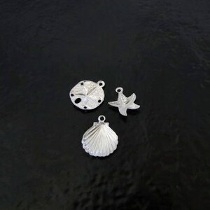May include: Three silver charms in the shape of a seashell, a starfish, and a sand dollar.