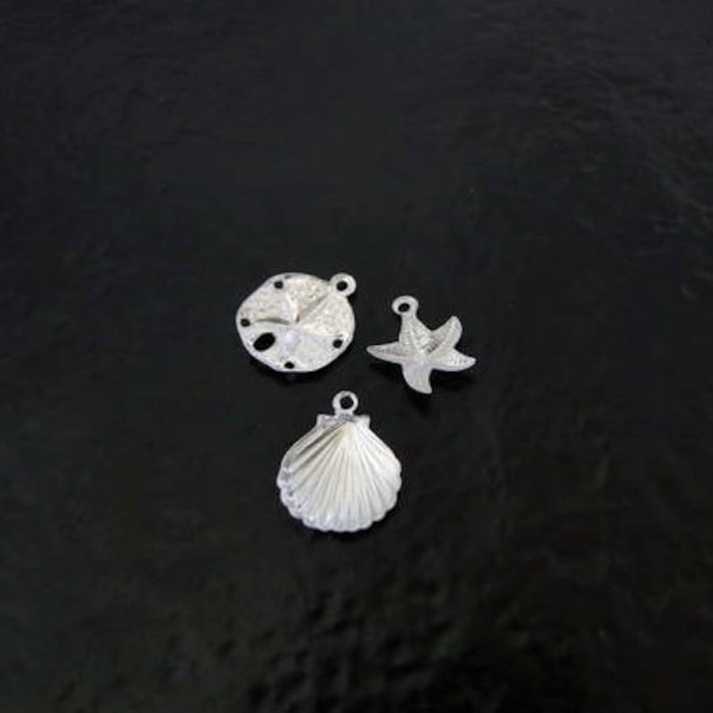 May include: Three silver charms in the shape of a seashell, a starfish, and a sand dollar.