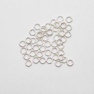 May include: A pile of silver jump rings, a type of jewelry finding used for connecting chains, cords, and other jewelry components.