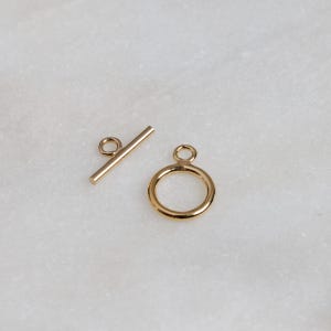 May include: Gold-toned metal toggle clasp with a round ring and a straight bar. The clasp is used for jewelry making.
