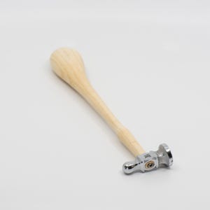May include: A wooden handled hammer with a round head and a silver finish. The hammer is designed for jewelry making.